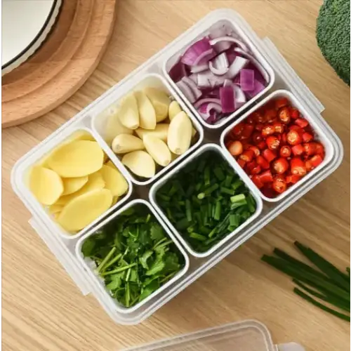 Clear plastic compartmentalized food storage container with six sections holding sliced onions, garlic cloves, ginger slices, chopped chives, cilantro, and red chili peppers.