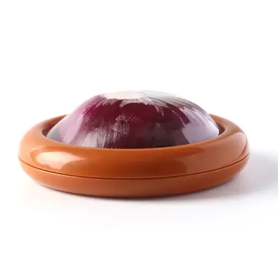 A glossy terracotta-colored onion slicer with a halved red onion resting inside its circular, ridged bowl.