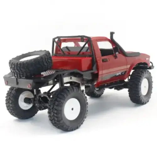 Red remote-controlled off-road pickup truck with black tires and white rims, featuring a spare tire mounted on the rear.
