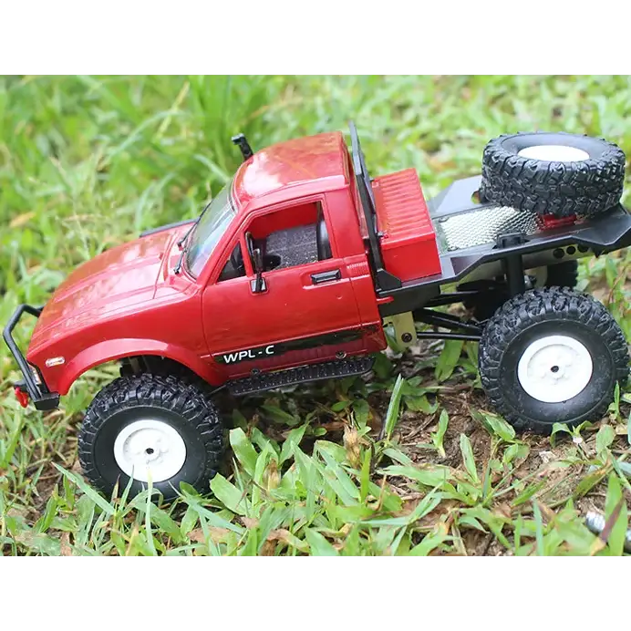 Red remote-controlled off-road truck with black tires and white rims, featuring a spare tire mounted on the bed.