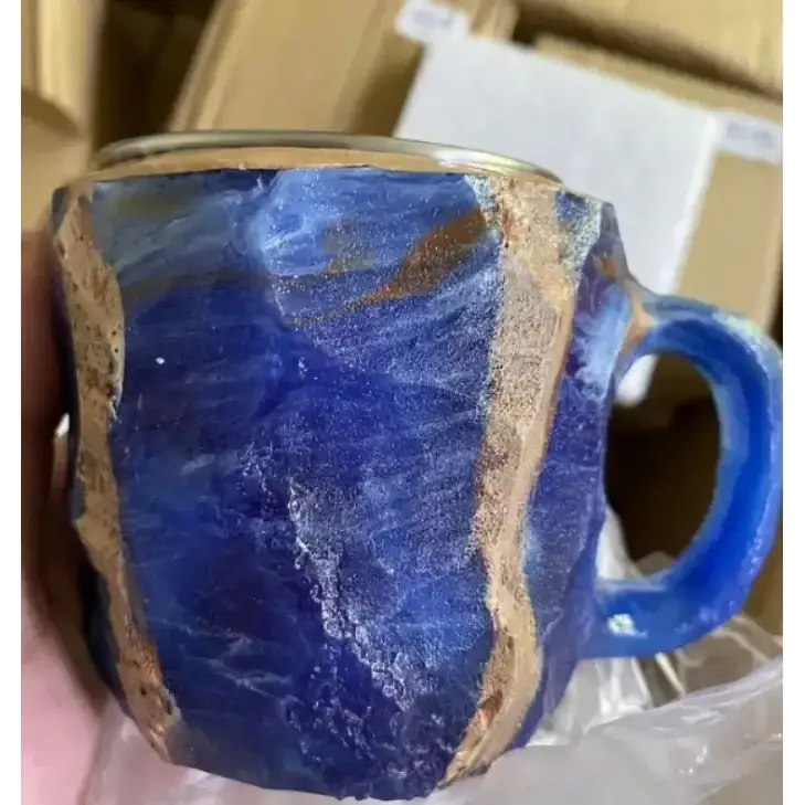 Handcrafted ceramic mug with a deep blue glaze and gold-colored accents along its irregular, textured edges.