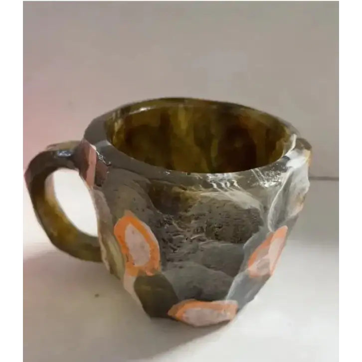 Handcrafted ceramic mug with a rugged, faceted exterior in earthy tones of gray and olive green, accented by orange and white circular patterns resembling natural stone or mineral deposits.