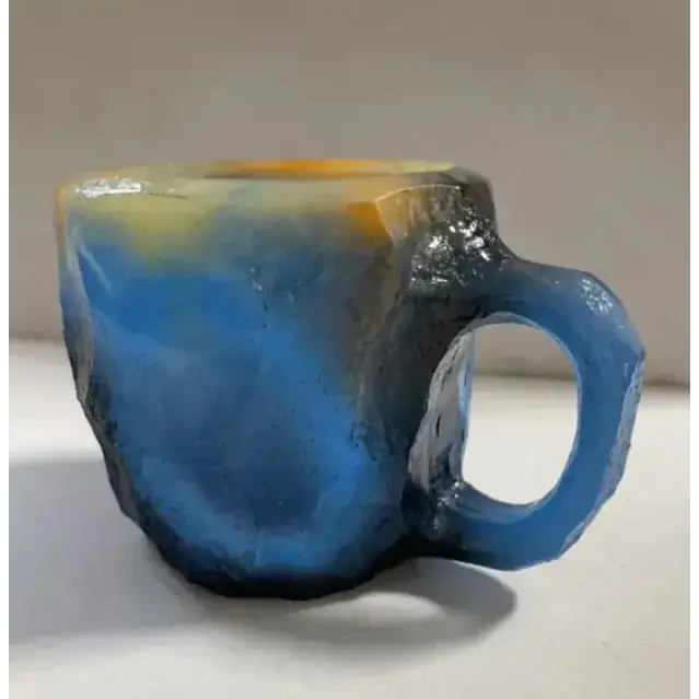 A handcrafted ceramic mug with a rugged, textured surface featuring swirling gradients of deep blue, yellow, and black.