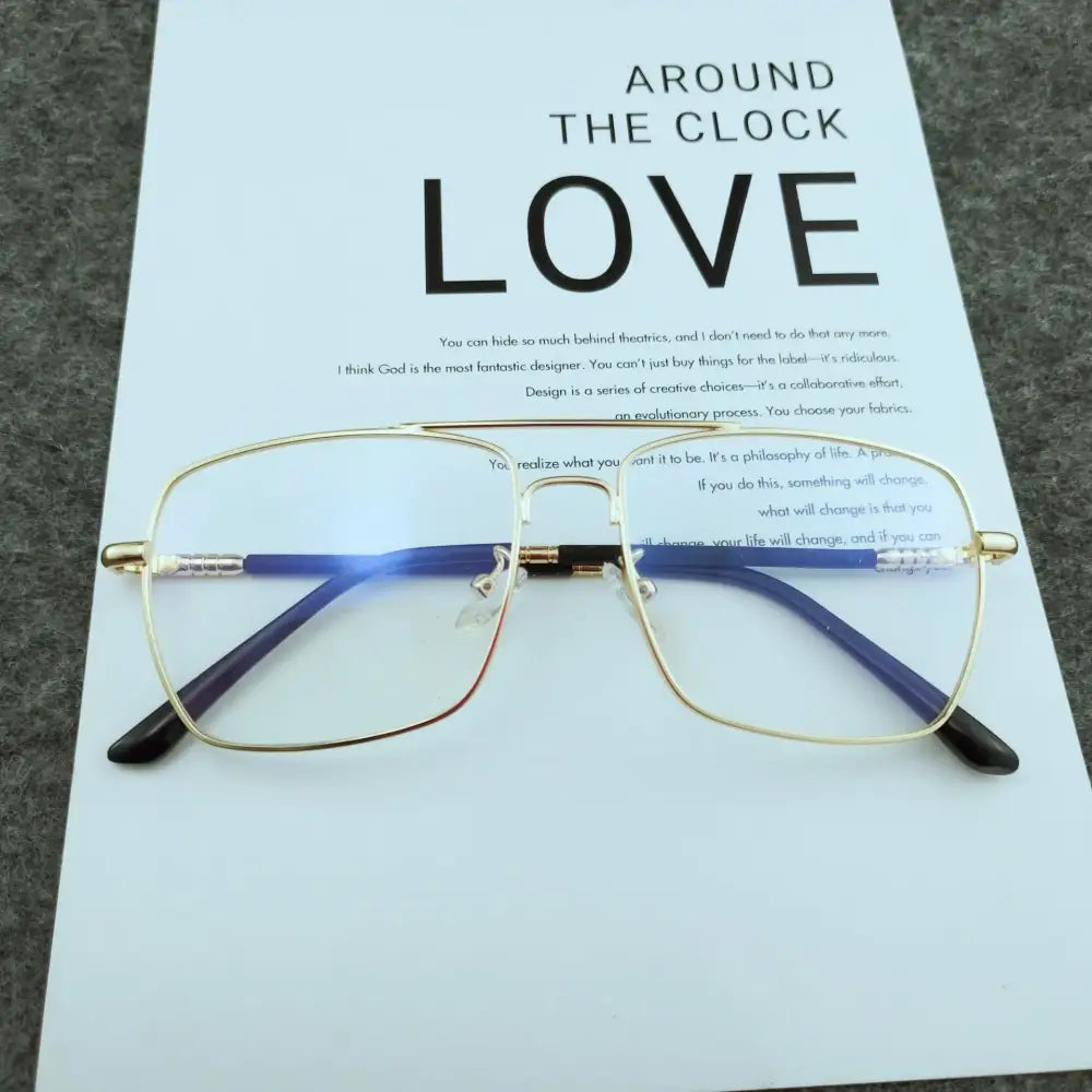 Gold-rimmed rectangular eyeglasses with blue temple arms and black tips, resting on a printed paper.