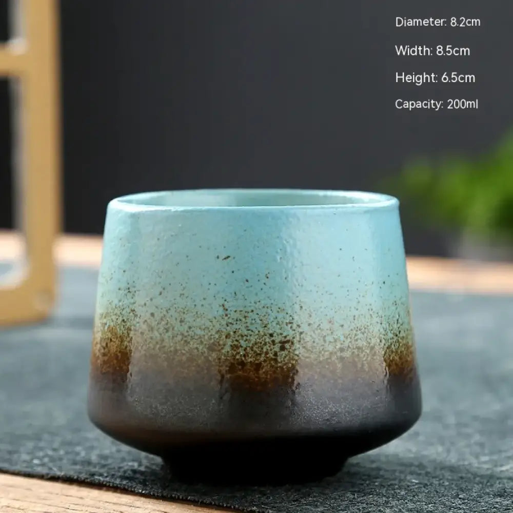 A handcrafted ceramic teacup with a gradient glaze transitioning from light blue to deep brown, featuring subtle speckles and a rustic, textured finish.