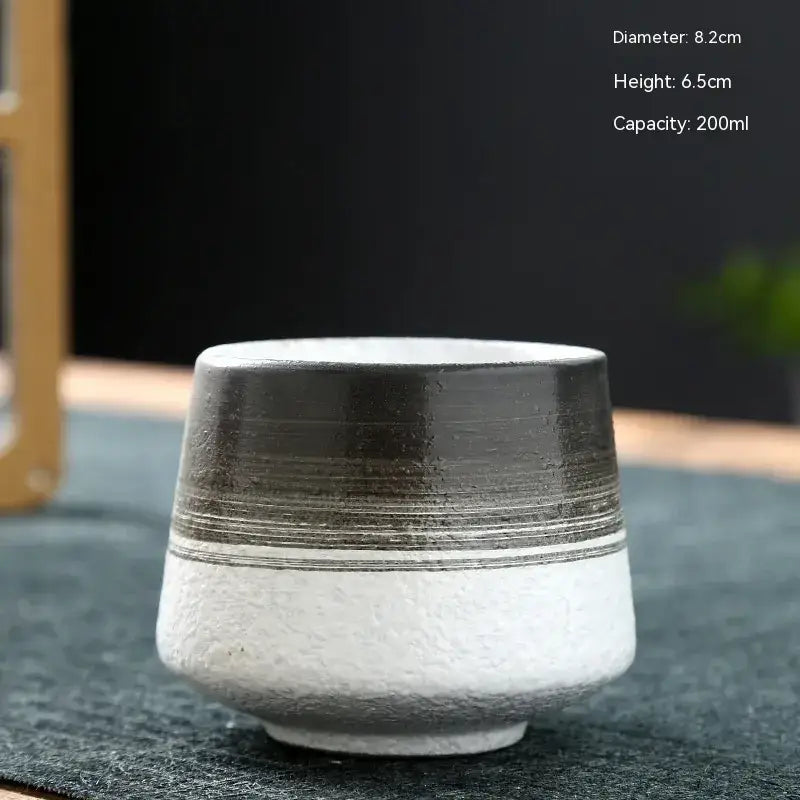 A ceramic tea cup with a textured white base and a dark gray upper section featuring horizontal striations.