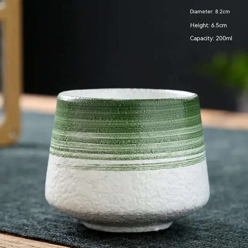 A ceramic tea cup with a textured white base and green horizontal stripes, featuring a rustic handmade finish.