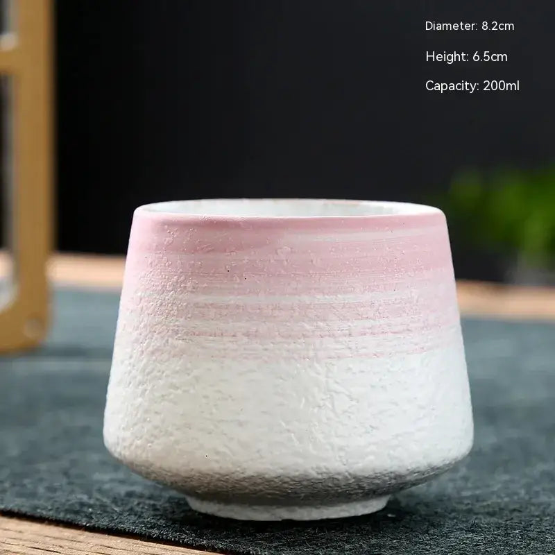 A handcrafted ceramic tea cup with a soft pink-to-white gradient glaze and textured surface, featuring dimensions of 8.2cm in diameter and 6.5cm in height, designed to hold 200ml.