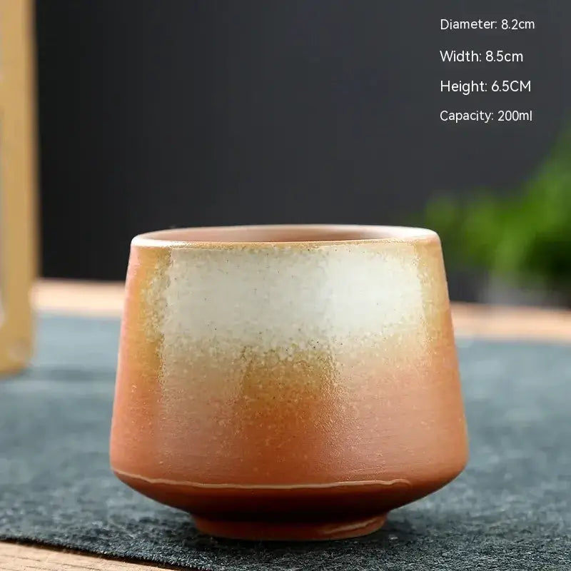 A rustic ceramic teacup with a gradient glaze transitioning from warm terracotta to creamy white, featuring subtle speckles and a slightly uneven rim.