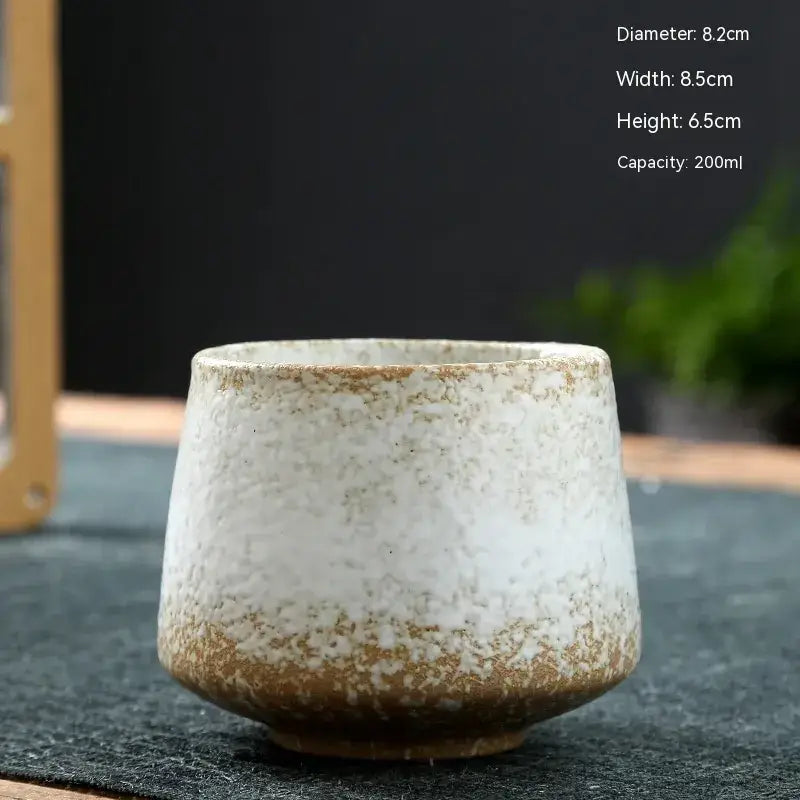 A rustic ceramic tea cup with a speckled white and brown glaze, featuring a wide rim and slightly tapered body.