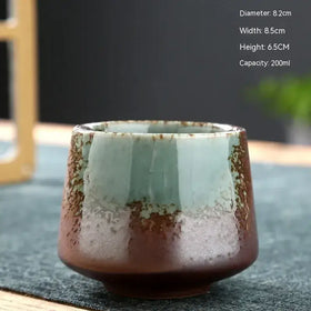 A handcrafted ceramic tea cup with a gradient glaze transitioning from muted teal to earthy brown, featuring subtle crackle texture and rustic imperfections.