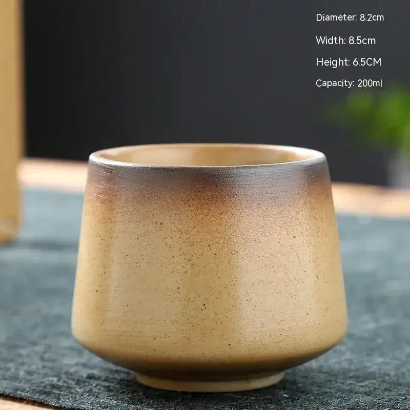 A handcrafted ceramic teacup with a smooth, speckled glaze that transitions from warm beige to deep brown at the rim.