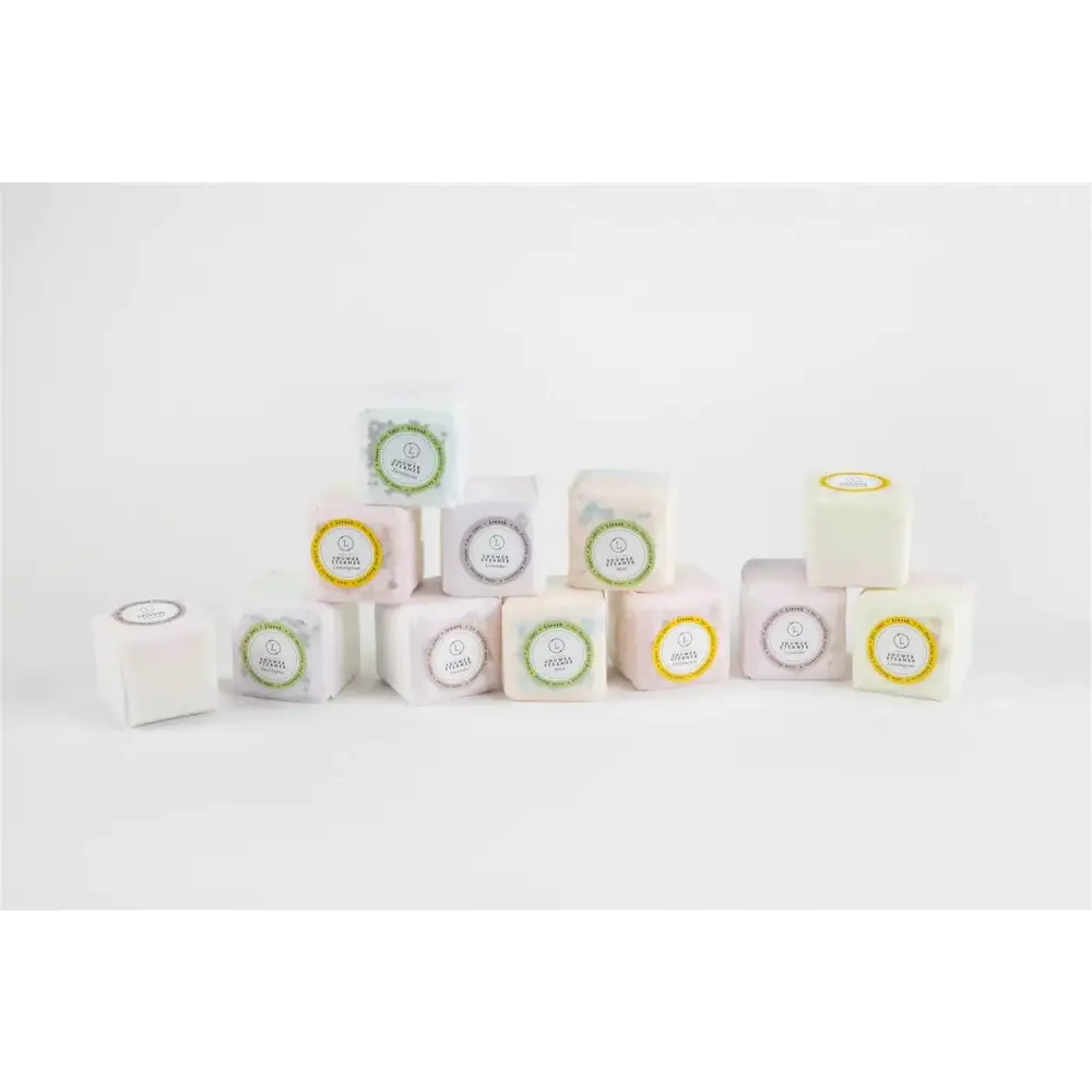 A collection of square-shaped, pastel-colored bath bombs in soft white, pink, and cream hues with decorative circular labels.