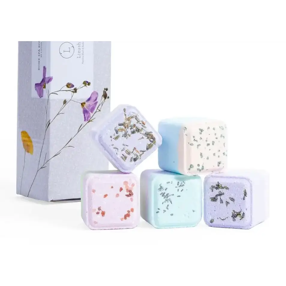 Pastel-colored square bath bombs with embedded dried flowers and herbs, presented in a minimalist box labeled ’home spa botanicals.’