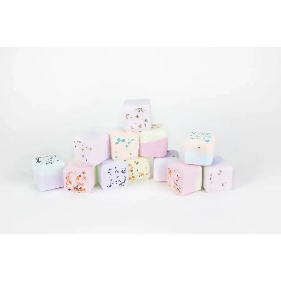 Pastel-colored bath bombs with speckled, glittery toppings in soft pinks, blues, and whites.