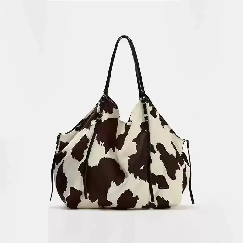 A black and white cow print tote bag with sleek, structured handles.