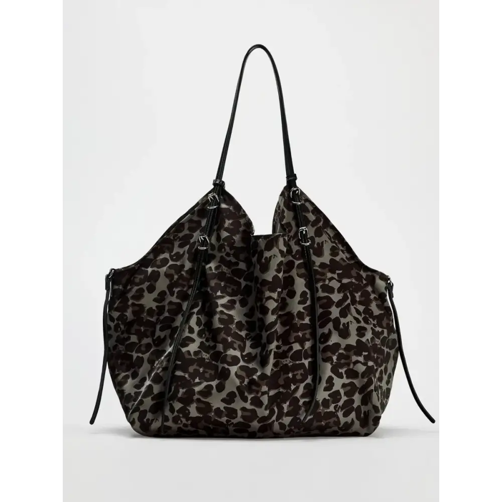 A sleek, oversized tote bag featuring a bold black and gray leopard print pattern on its fabric body with contrasting black leather straps.