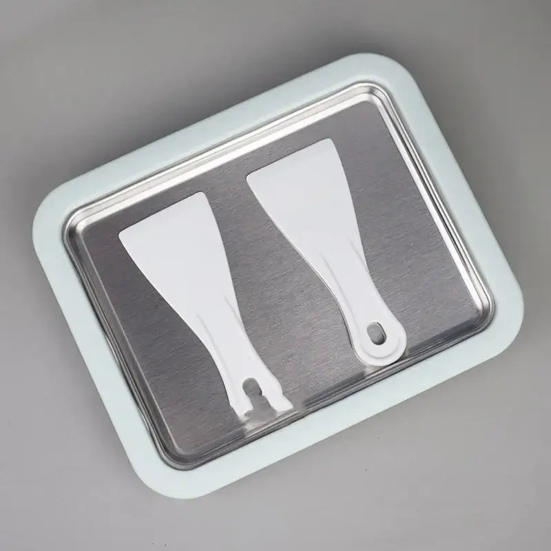 Light blue rectangular tray with a stainless steel interior holding two white plastic spatulas.