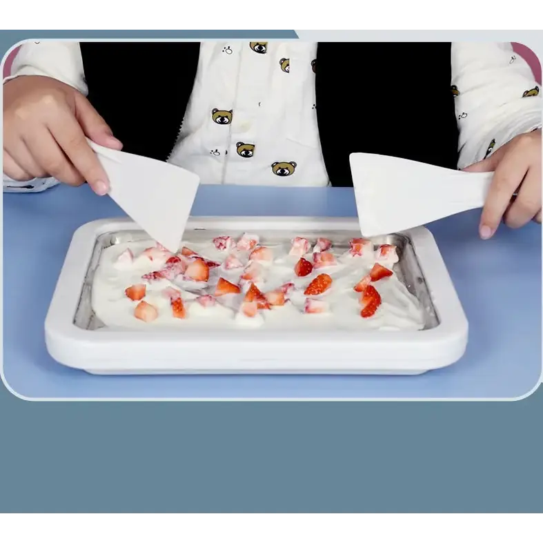 White rectangular ice cream maker with a chilled surface and strawberry pieces scattered on top.