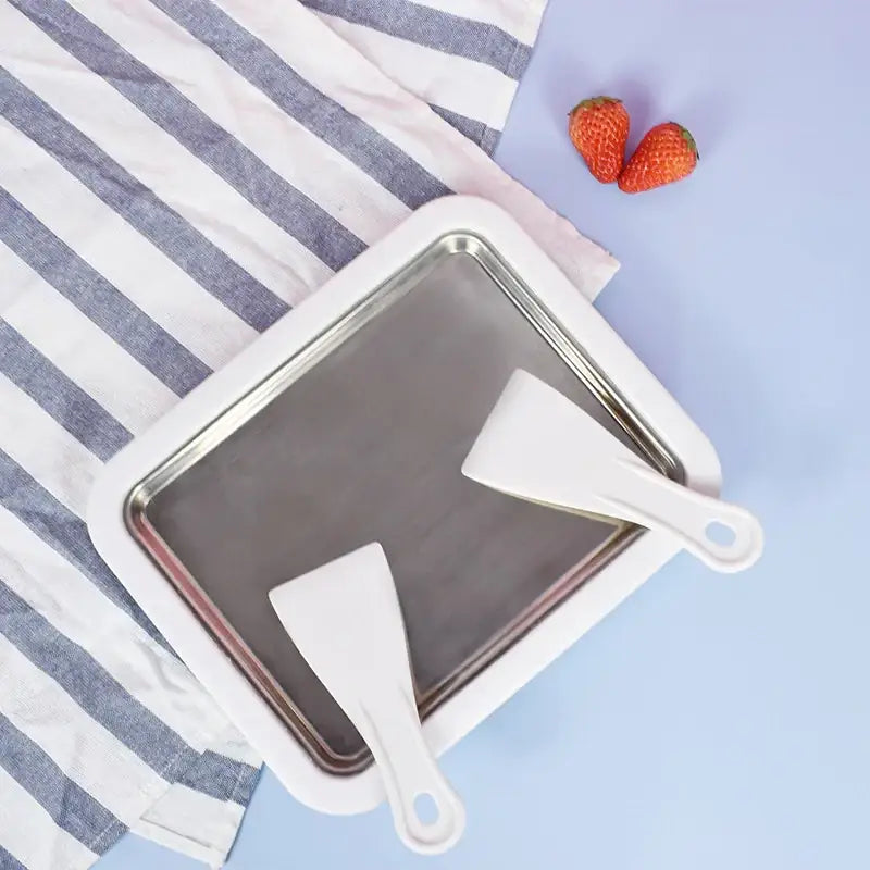 White rectangular ice cream making tray with stainless steel interior and two white plastic spatulas