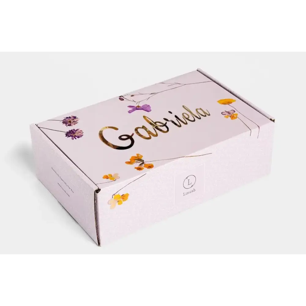 A delicate lavender-colored cardboard box adorned with gold foil lettering and a floral design featuring purple and yellow blossoms.