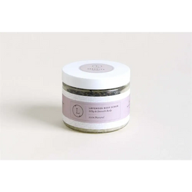 A lavender-scented body scrub in a clear glass jar with a white lid and purple label, featuring the brand name ’serenity’ and the text “100% natural.”
