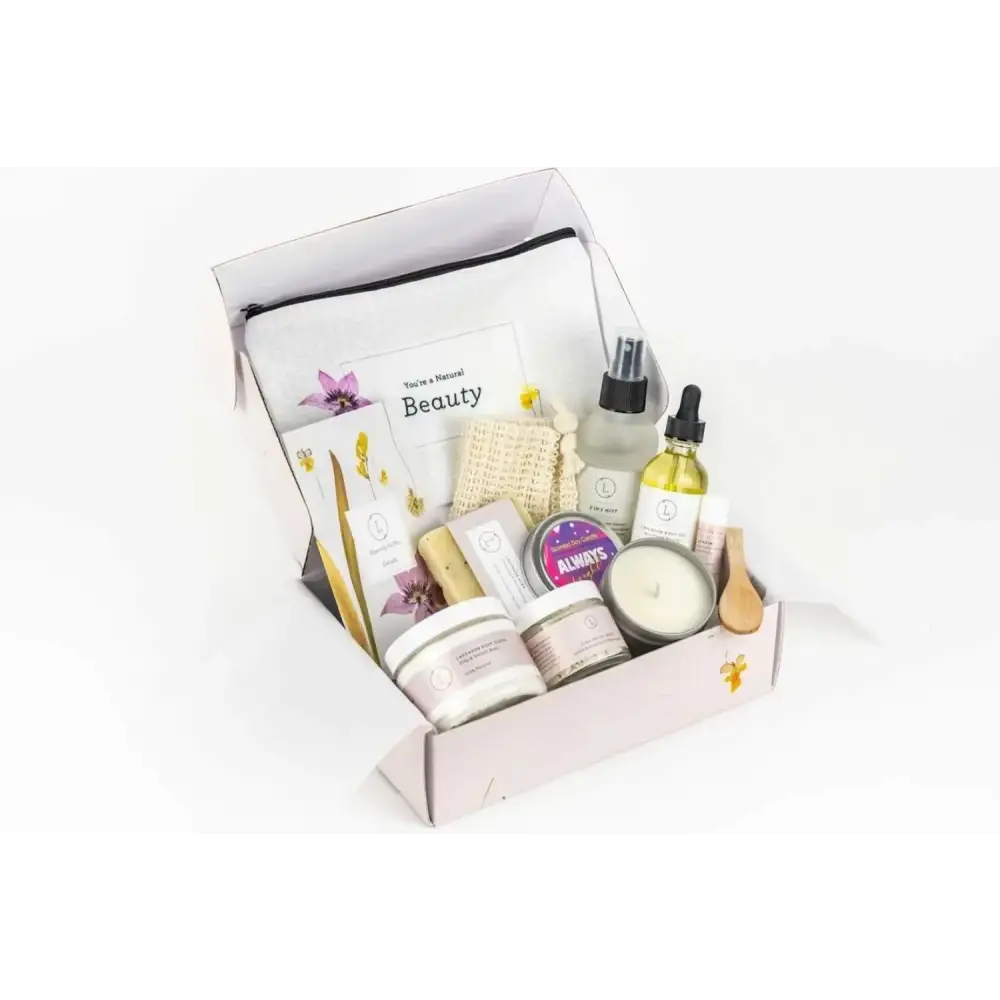 A pale pink gift box filled with assorted natural beauty products, including candles, lotions, and essential oils.