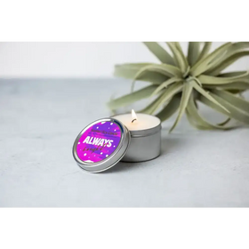 A lit, silver tin candle with a vibrant purple lid featuring the phrase ’always bright’ in white and gold lettering.
