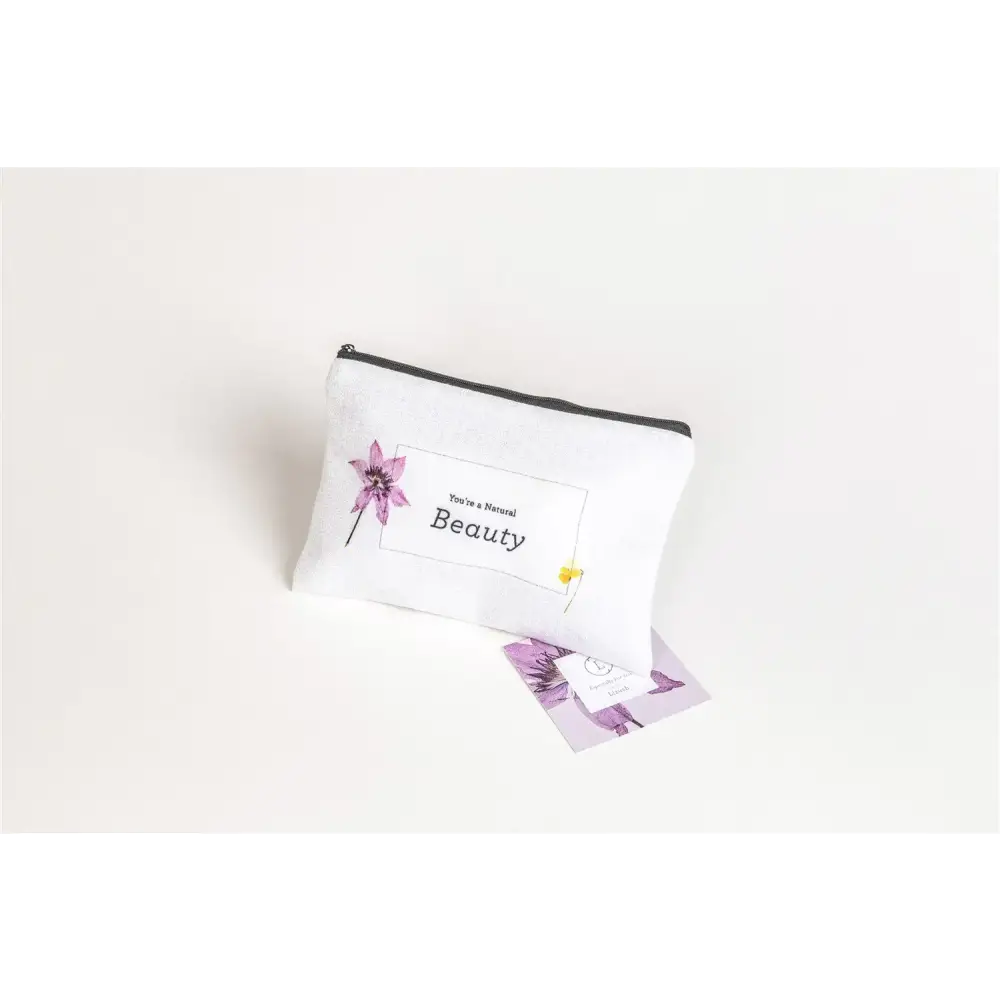 White fabric pouch with black zipper, featuring a purple flower illustration and the text ’you’re a natural beauty’ in a rectangular frame.
