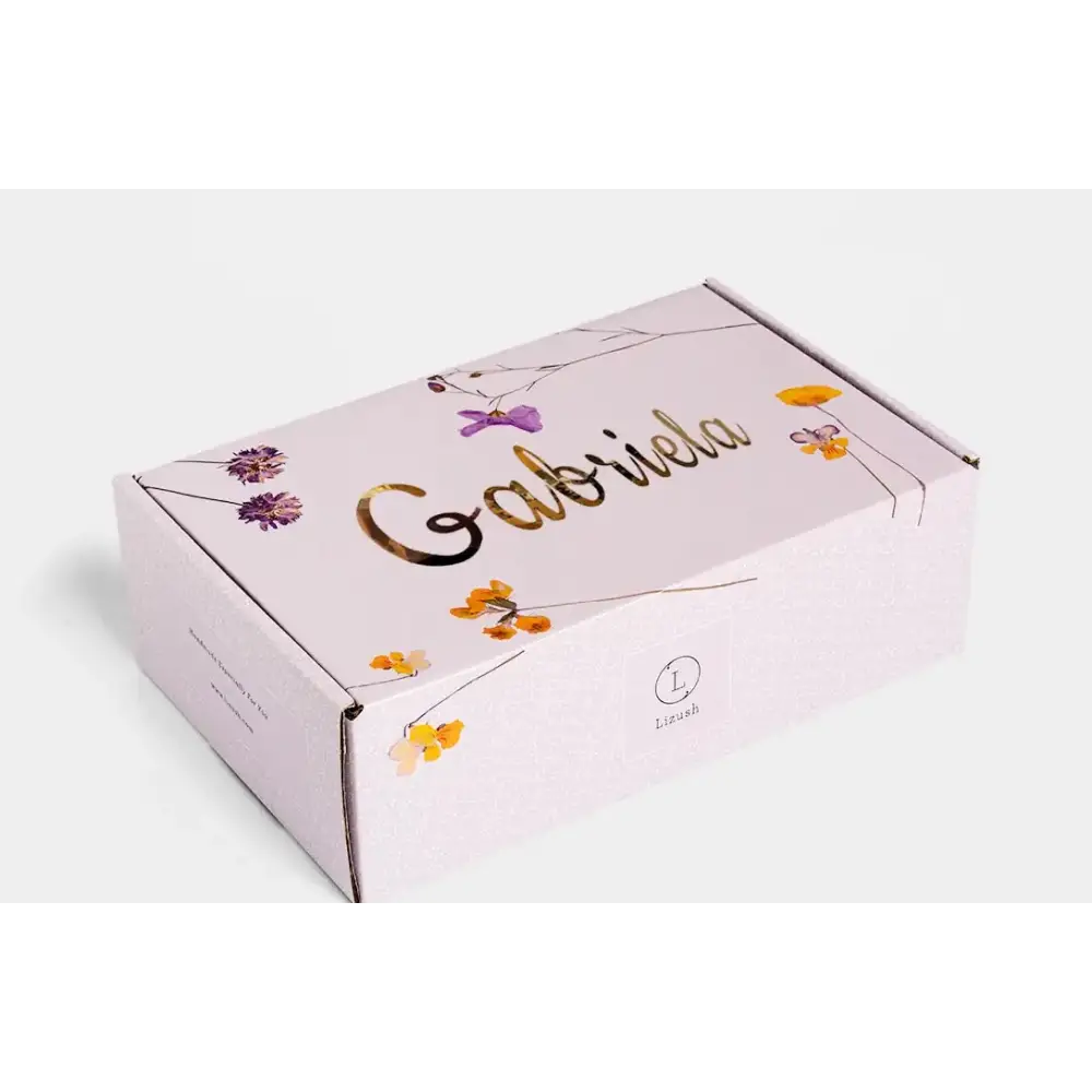 A delicate lavender-colored cardboard box adorned with gold foil lettering and a floral design featuring purple and yellow blossoms.