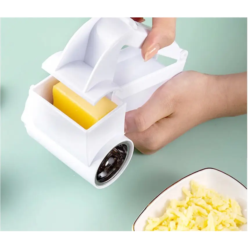 White plastic cheese grater with a yellow block of cheese inside and shredded cheese in a bowl nearby