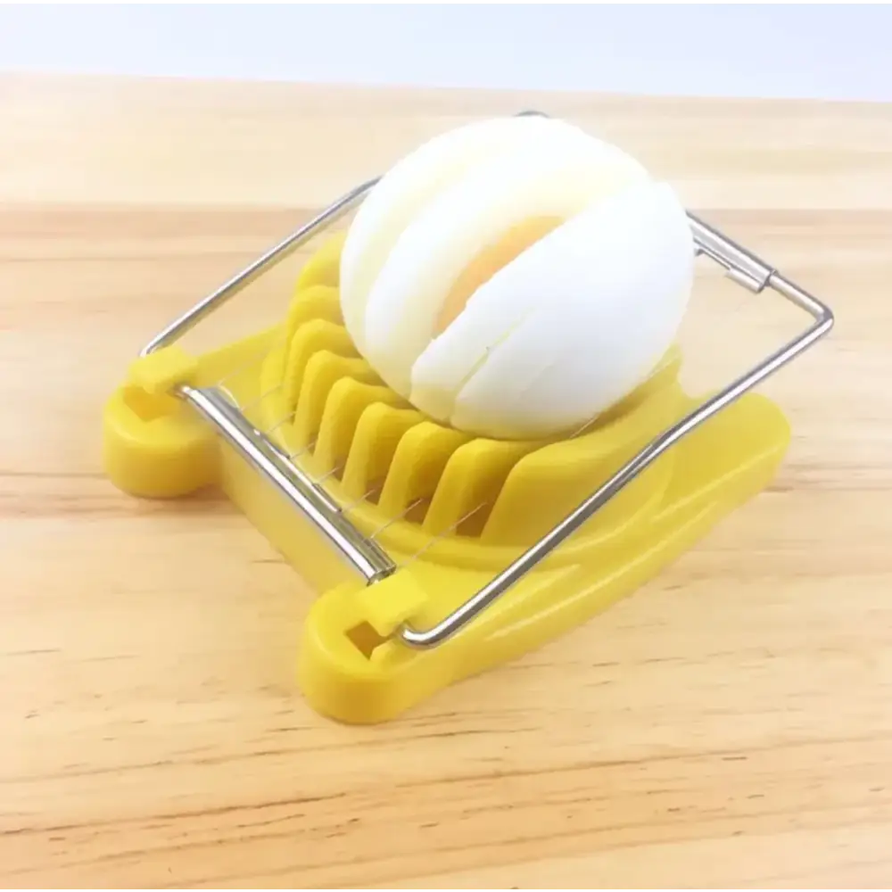 Yellow plastic egg slicer with metal frame slicing a hard-boiled egg into even slices.