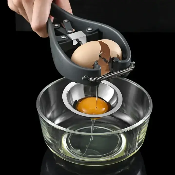 Black plastic and stainless steel egg separator with a spring-loaded mechanism holding an egg as the yolk drips into a glass bowl below.