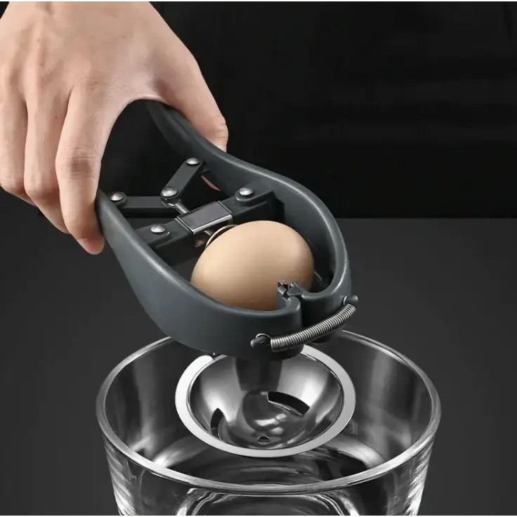 Black plastic egg cracker with a spring-loaded mechanism holding a brown egg above a stainless steel bowl.