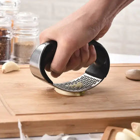 Stainless steel garlic press with black ergonomic handles, featuring a perforated grinding surface for easy mincing.