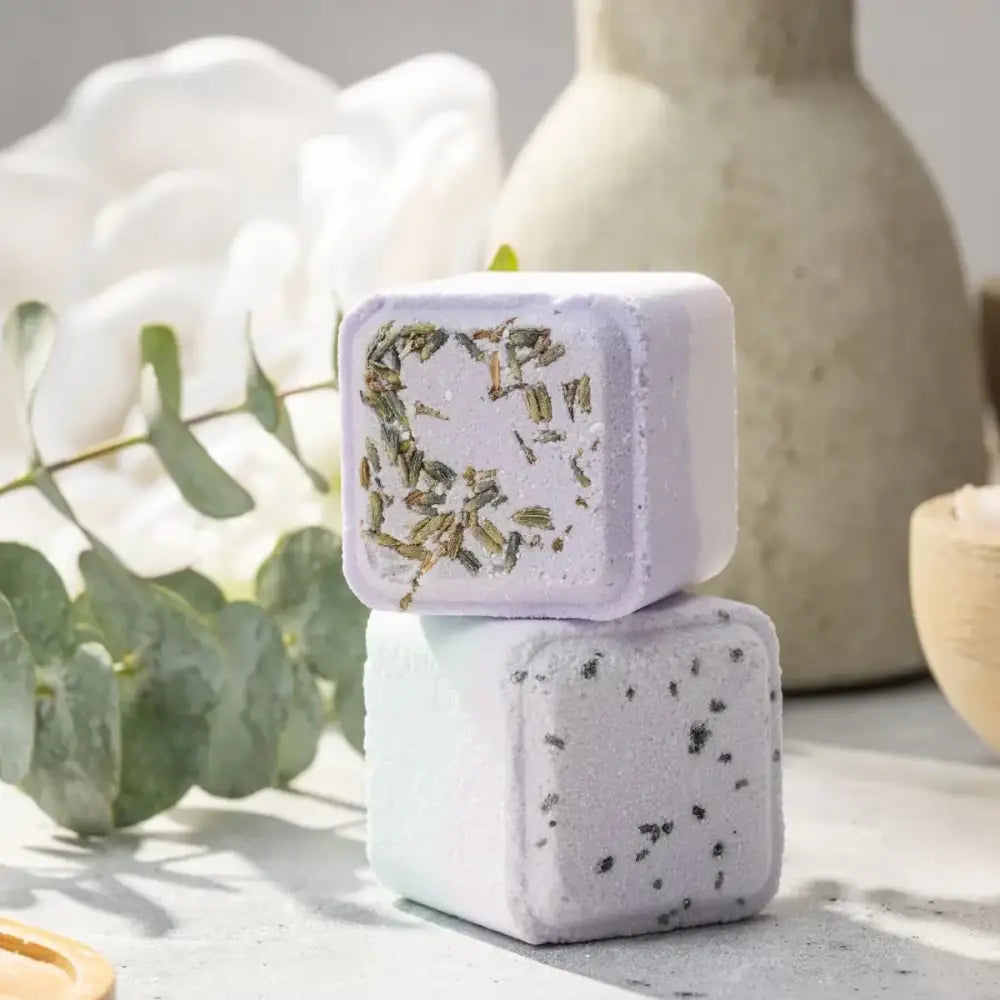 Two lavender-scented bath bombs, one with dried herbs embedded in a soft purple hue and the other speckled with dark flecks.