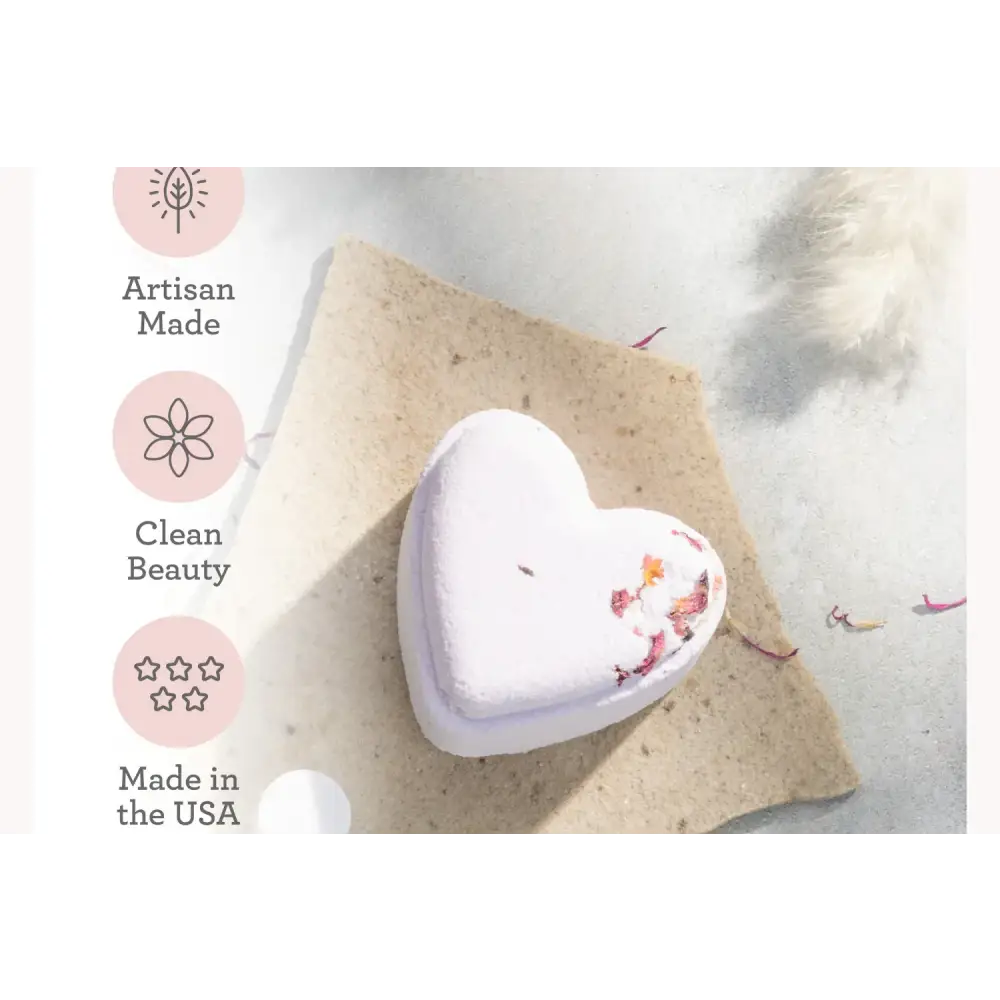 A lavender heart-shaped bath bomb with dried flower petals embedded in its surface.