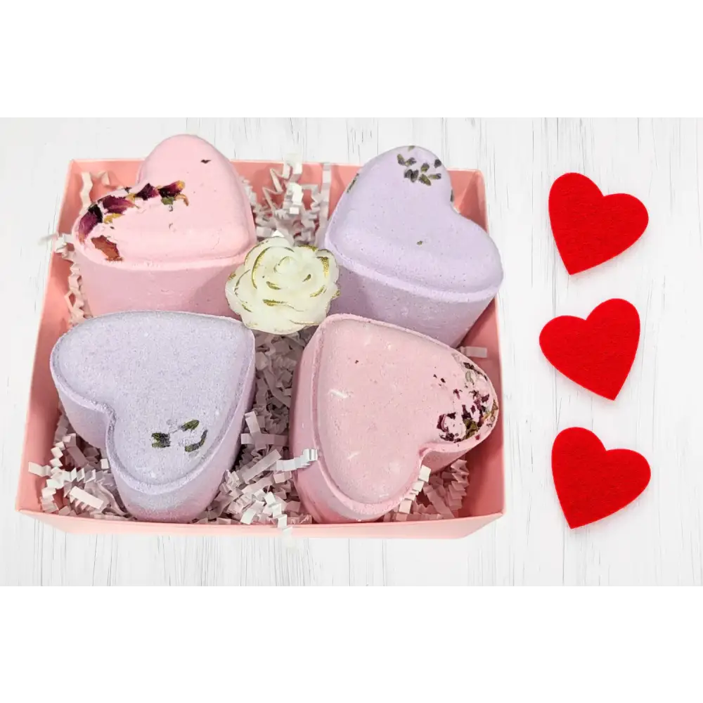 Pink and lavender heart-shaped bath bombs with dried flower accents nestled in a pink gift box.