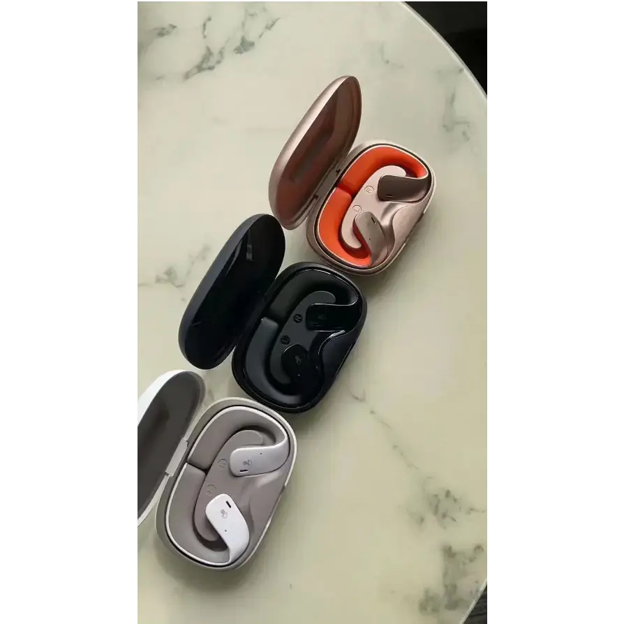 Three pairs of wireless earbuds in sleek, minimalist cases—rose gold with orange interior lining, black, and gray—with matching curved earpieces designed for a secure fit.
