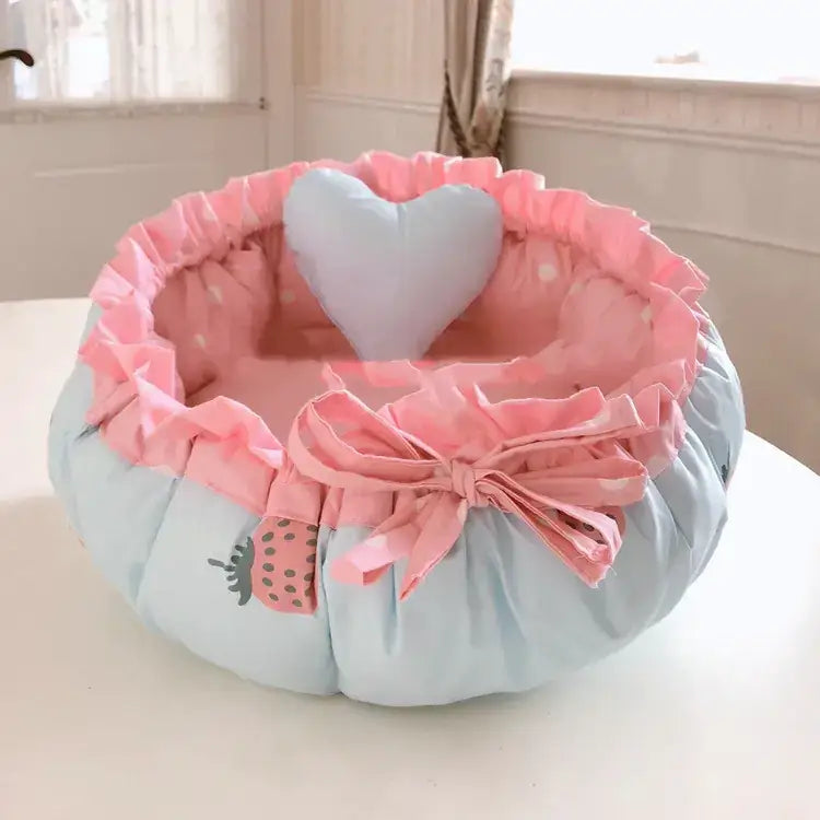 Pastel blue and pink ruffled pet bed with a strawberry print, heart-shaped pillow, and bow.
