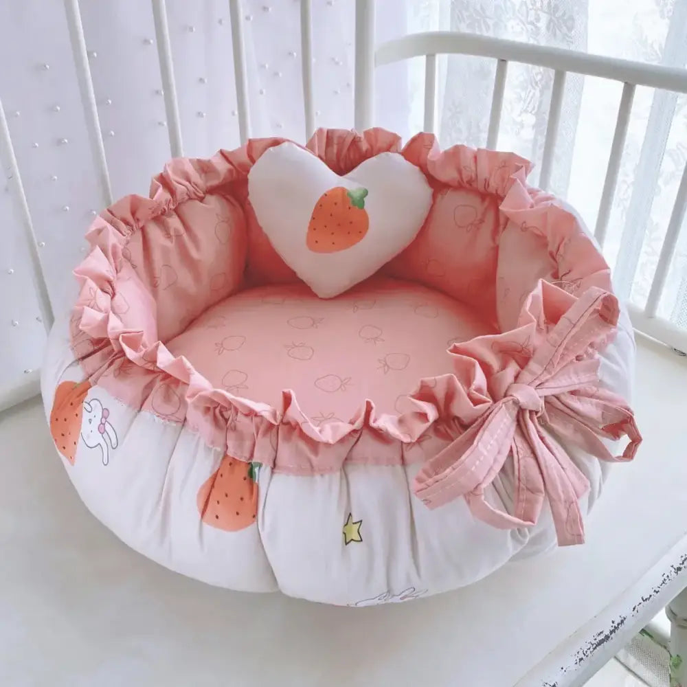 Pink and white strawberry-themed pet bed with ruffled edges and a heart-shaped pillow.