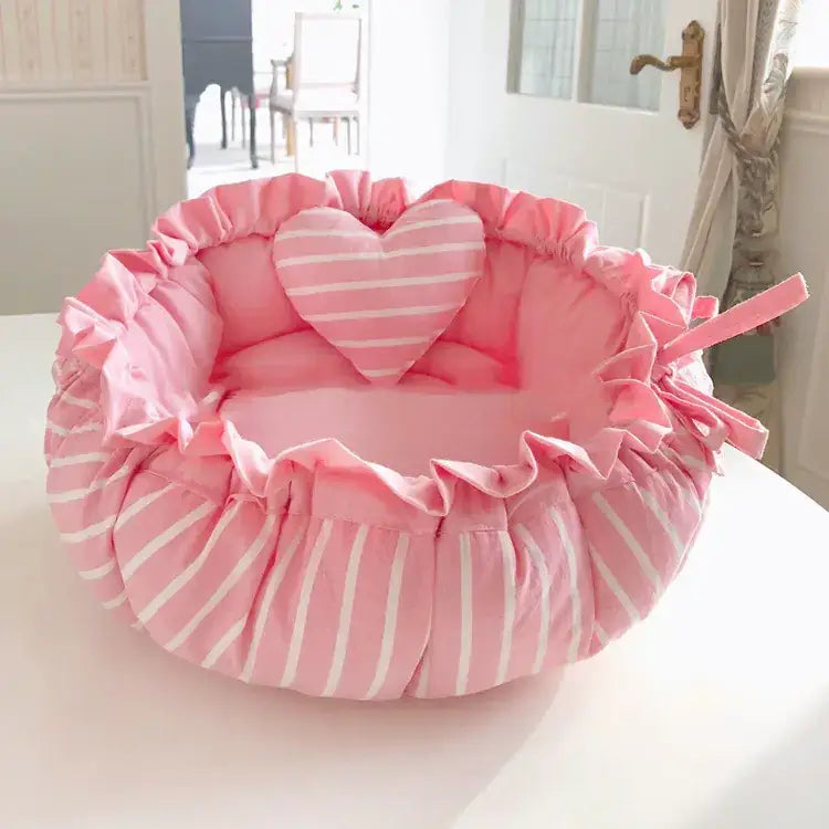 Pink and white striped ruffled pet bed with a matching heart-shaped pillow inside.
