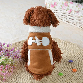 Brown fluffy dog wearing a tan suede vest with white faux fur trim and large white toggle closures.