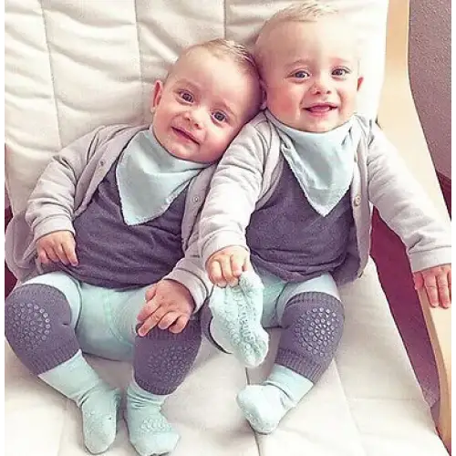 Two identical twin babies, dressed in matching gray and light blue outfits with soft fabric textures.