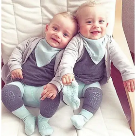 Two identical twin babies, dressed in matching gray and light blue outfits with soft fabric textures.