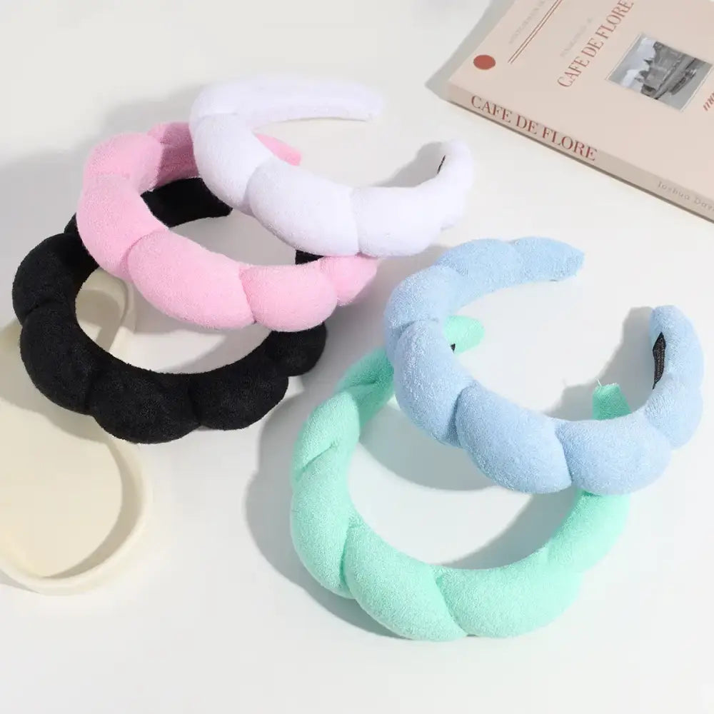 Soft, plush pastel-colored headbands in pink, white, black, light blue, and mint green with a quilted texture.