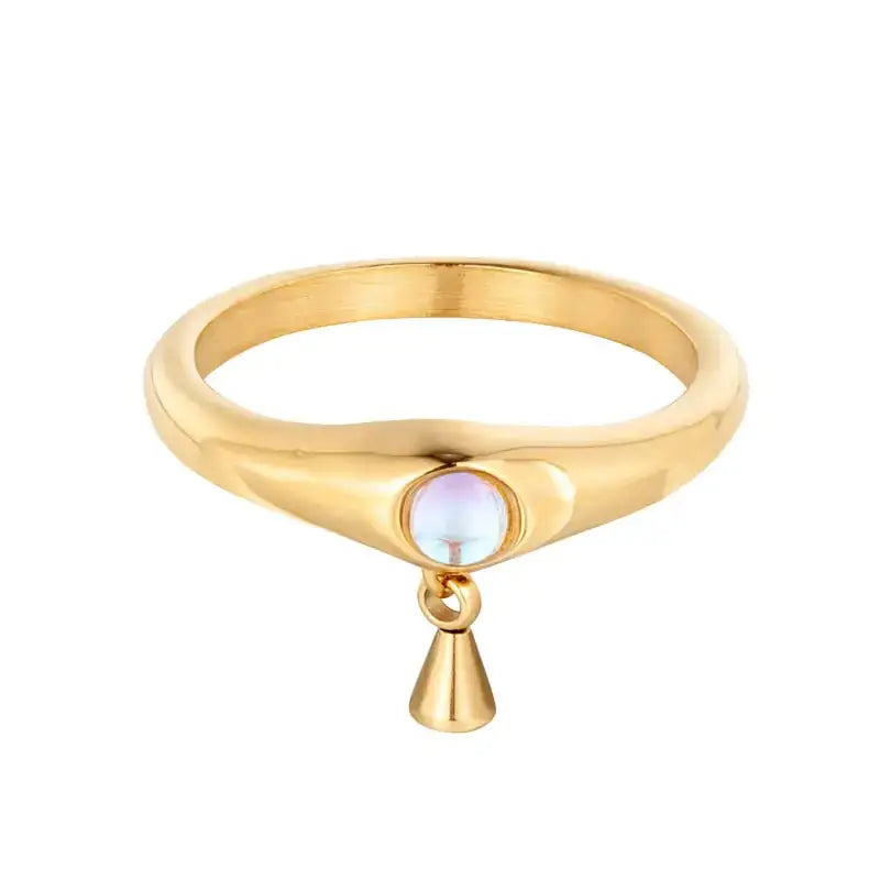 Gold-toned ring featuring a smooth, rounded band with an oval-shaped iridescent stone set at the center and a small dangling cone pendant below.