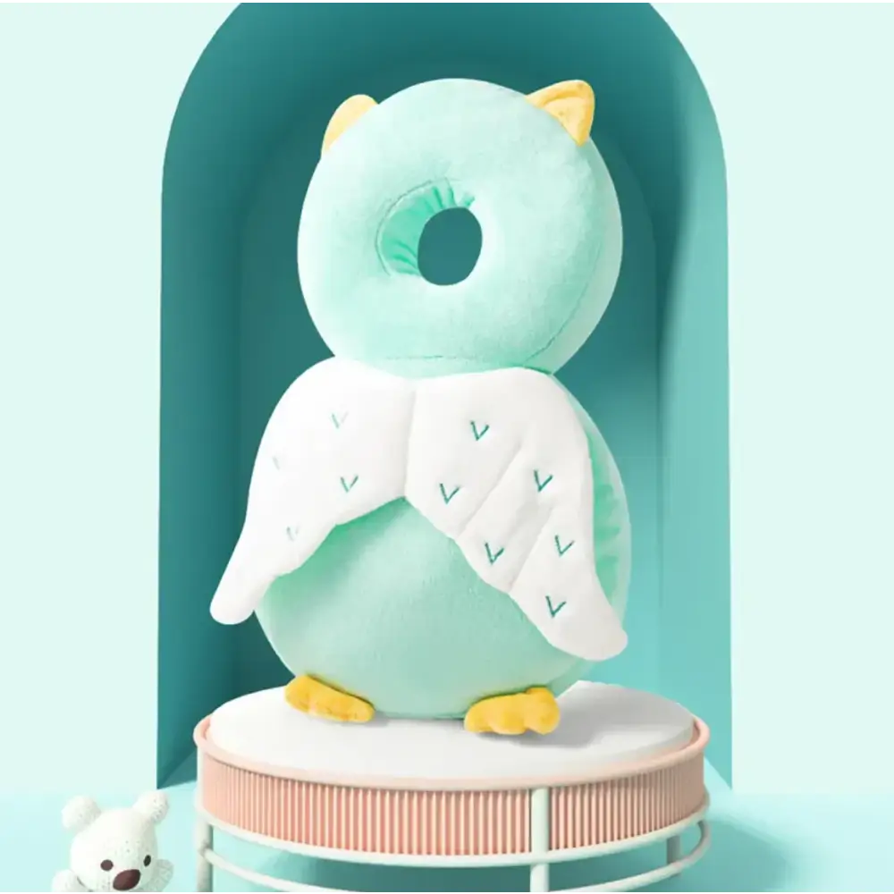 A soft mint green plush owl-shaped baby back support with white angel wings embroidered with teal chevrons and yellow feet.