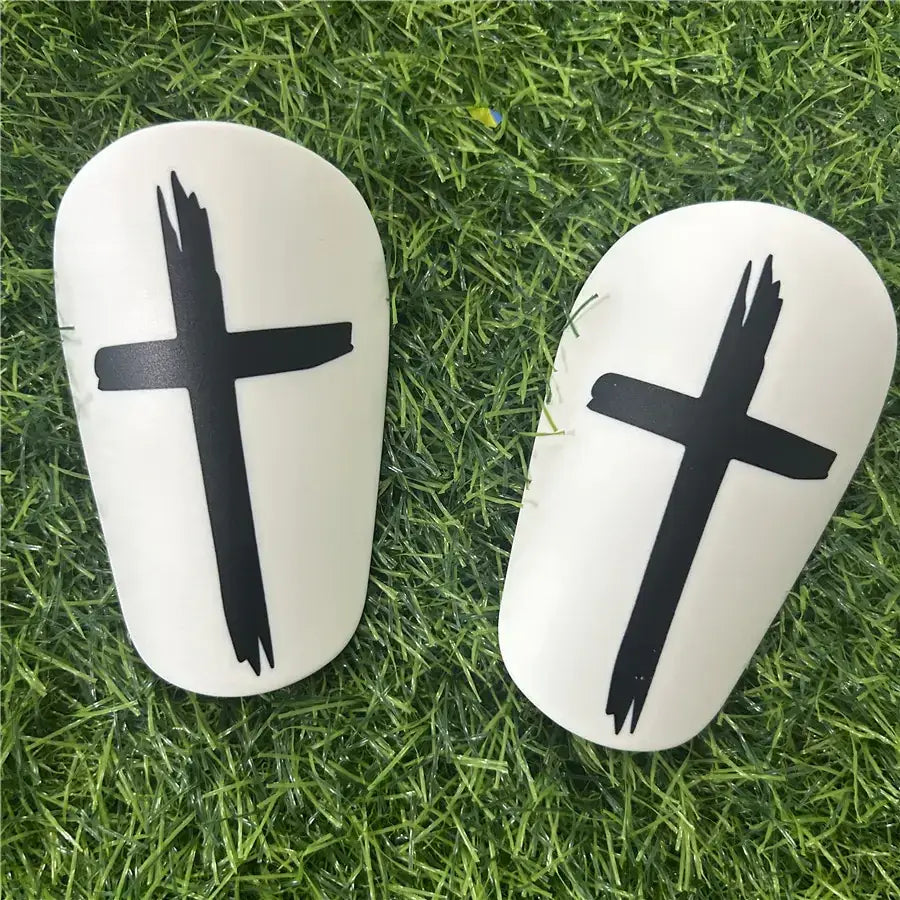 White soccer shin guards with black cross decals.