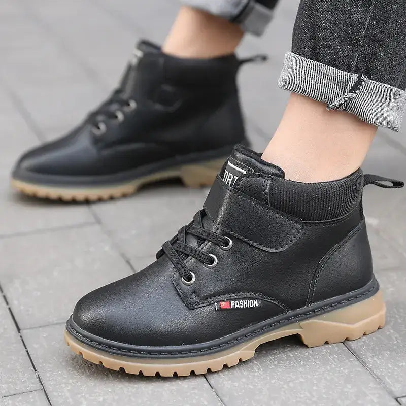 Black leather ankle boots with a tan rubber sole and velcro strap closure.